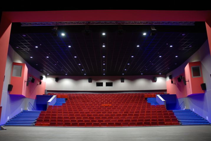 Zdjęcie przedstawiające wnętrze sali kinowo-widowiskowej MOK Międzyrzecz. Zdjęcie wykonane zostało od strony sceny. Sala wypełniona jest rzędami czerwonych foteli kinowych. Po obu stronach sali prowadzą do nich rzędy podświetlonych ledami schodów.